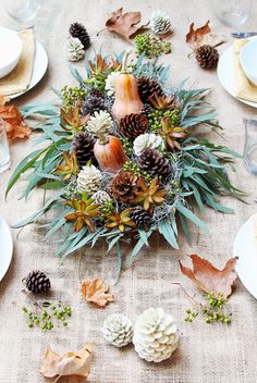 an arrangement of pine cones and succulents on a linen tablecloth with place settings