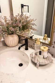 a white sink sitting under a bathroom mirror next to a vase with flowers in it