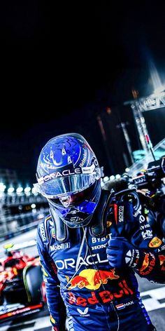 a man with a helmet on standing in front of a red bull racing car at night