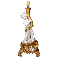 a white and gold statue with a yellow candle on it's base, holding a snake