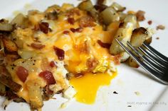 a white plate topped with hash browns covered in cheese and bacon next to a fork