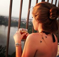 a woman with tattoos on her back drinking from a beer glass in front of a balcony