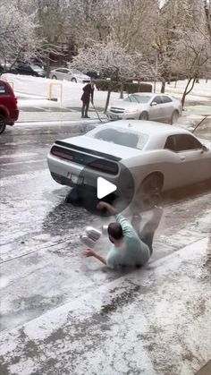 a man kneeling down next to a car in the street with snow all over it