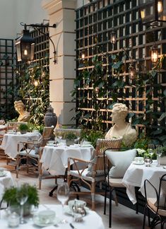 an indoor restaurant with tables and chairs covered in white tablecloths, surrounded by greenery