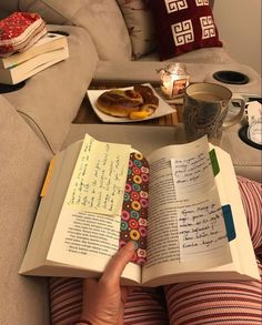 a person is reading a book on the couch with food and drinks in the background