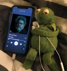 a stuffed animal with headphones next to an mp3 player on a bed in front of a cell phone