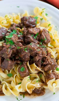 a white plate topped with pasta covered in meat and gravy on top of a wooden table