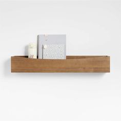 a wooden shelf with two notebooks and a notepad on the top, in front of a white wall