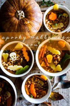 four white bowls filled with soup and vegetables on top of a wooden table next to pumpkins