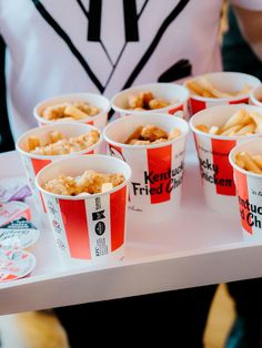 several buckets of fried chicken and fries on a table with people in the background