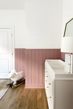 a white dresser sitting next to a pink wall in a room with wooden floors and walls