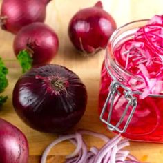 red onions and other vegetables on a cutting board next to a jar of pickled onion