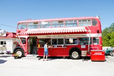 a red double decker bus parked in front of a building with people standing outside it