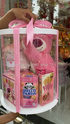 a pink teddy bear in a clear case with candy and other items on display at a store