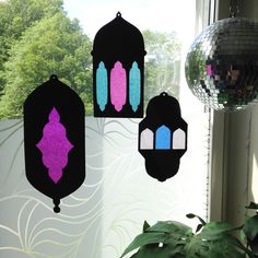 three decorative hangings in front of a window with disco ball and mirror behind them