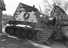 an old tank is sitting in the dirt near a building and tree stumps on it's side