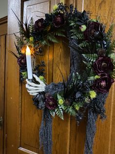 a wreath with flowers and a lit candle on the front door to a house that has been decorated for halloween