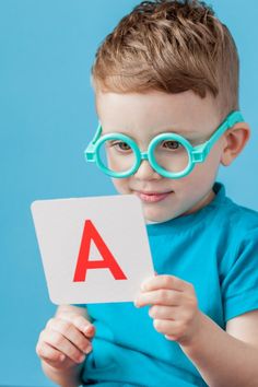 a young boy wearing glasses and holding up a card with the letter a on it