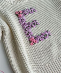 a white sweater with pink and purple flowers embroidered on the front, sitting on a table