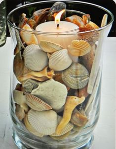 a candle that is inside of a glass vase filled with seashells and sea shells