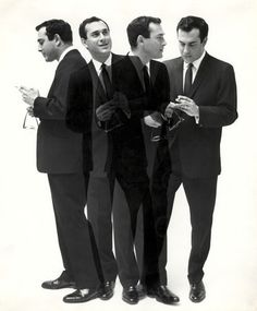 three men in suits standing next to each other and one is holding a cell phone