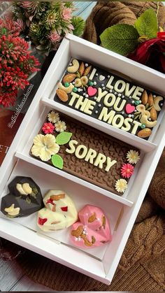 three decorated donuts in a white box with the words i love you most and sorry written on them