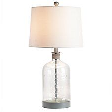 a clear glass lamp with a white shade on the base and a silver metal base