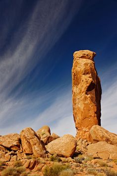 a large rock formation in the middle of some rocks and grass under a blue sky with wispy clouds