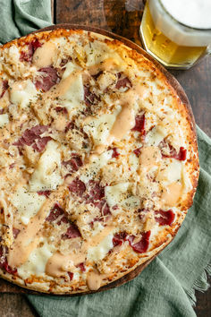 a pizza sitting on top of a wooden table next to a glass of beer and napkin