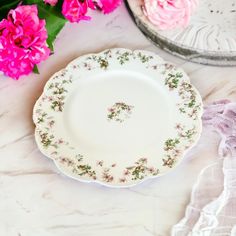 a white plate with pink flowers on it next to a glass container and napkins