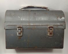 an old metal box with two handles on the top is sitting against a white wall