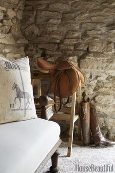 a room with a couch, horse saddle and boots on the floor in front of a stone wall