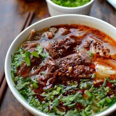 a bowl filled with meat and vegetables on top of a wooden table next to other bowls