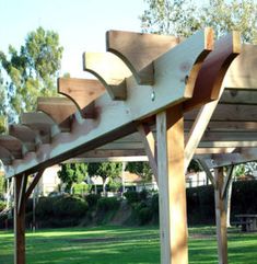 a wooden bench sitting under a pergolated covered area in a park with green grass and trees