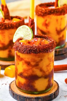 two glasses filled with yellow liquid and topped with a lime slice, sitting on a wooden plate