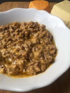 a white bowl filled with meat and cheese on top of a wooden table next to crackers