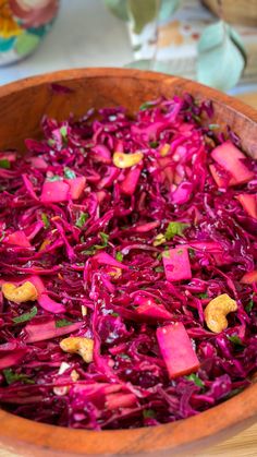 a wooden bowl filled with red cabbage and chopped carrots on top of a table