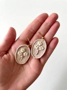 a pair of earrings with daisies in the shape of oval cabochons on a person's hand