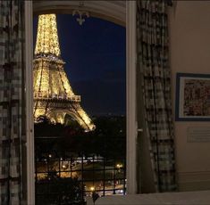 the eiffel tower lit up at night seen through an open window with curtains