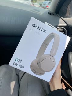 a person holding up a sony headphones in their car