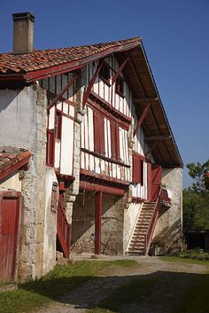 an old building with red and white shutters next to a stone path in front of it