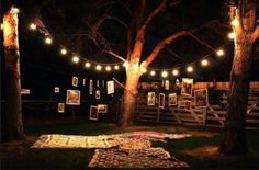 an outdoor area lit up with string lights and pictures on the wall, surrounded by trees