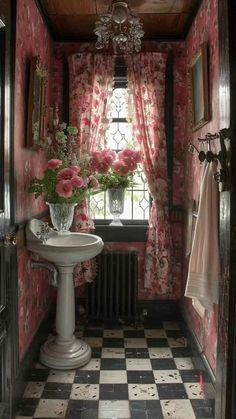 a bathroom decorated in pink and white with flowers on the window sill, sink and mirror