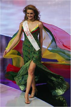 a woman in a green dress is walking down the runway with a sash around her neck