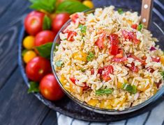 a bowl filled with rice and vegetables on top of a table next to some tomatoes