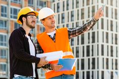 two men in hard hats and safety vests standing next to each other