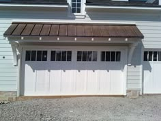 a white garage with two windows and a brown roof