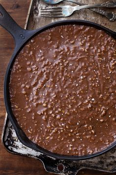 a cast iron skillet filled with chocolate pudding on top of a wooden table next to utensils