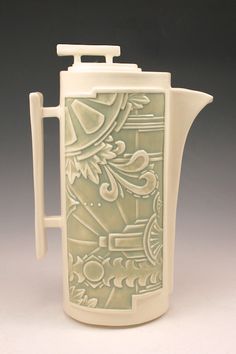 a white pitcher with an ornate design on the front and sides, sitting against a gray background