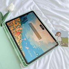 an open tablet computer sitting on top of a bed next to a white tulip